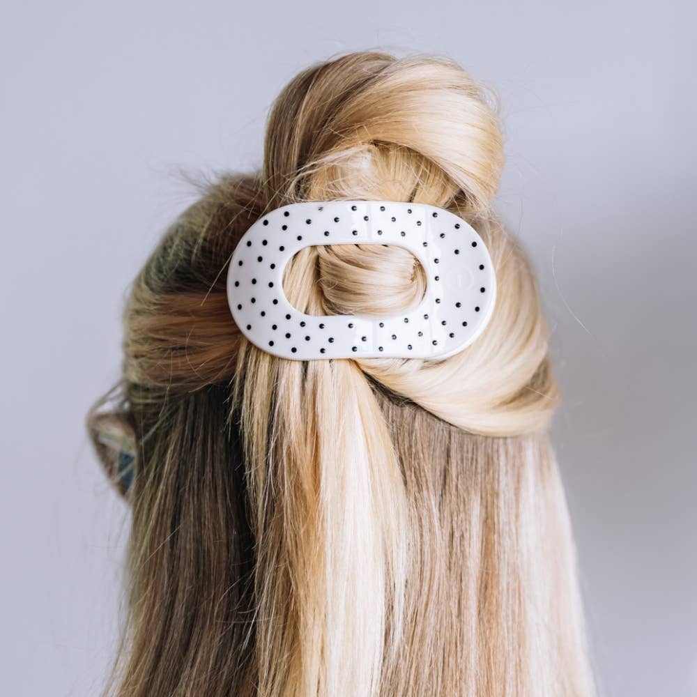 A white hair claw clip with black polka dots, shown holding up a blonde and brown half-up hairstyle on a model's head against a light gray background.