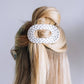 A white hair claw clip with black polka dots, shown holding up a blonde and brown half-up hairstyle on a model's head against a light gray background.