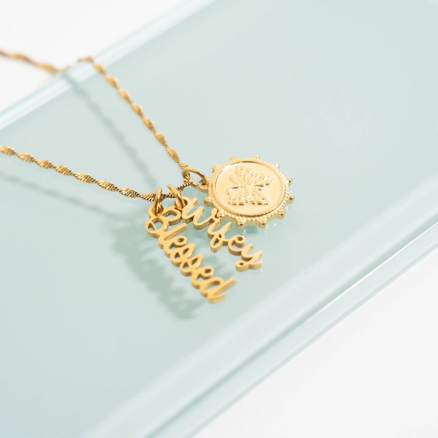 Gold necklace with 'blessed' pendant on a light green background
