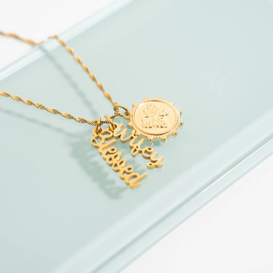 Gold necklace with 'blessed' pendant on a light green background