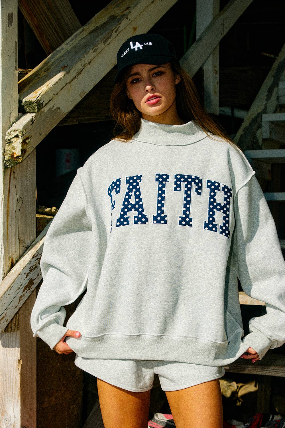 Person wearing a gray sweatshirt with 'FAITH' text and a black cap indoors.