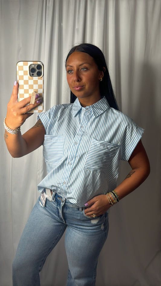 A woman takes a mirror selfie wearing a light blue and white vertically striped short-sleeve button-up shirt with chest pockets, paired with light-wash blue jeans.