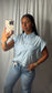 A woman takes a mirror selfie wearing a light blue and white vertically striped short-sleeve button-up shirt with chest pockets, paired with light-wash blue jeans.