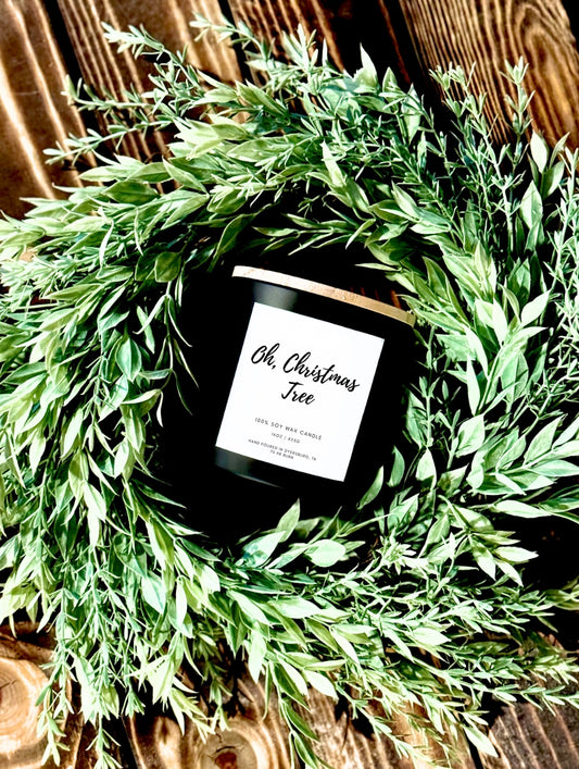 Candle labeled 'Oh, Christmas Tree' on a decorative green wreath with a wooden background