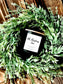 Candle labeled 'Oh, Christmas Tree' on a decorative green wreath with a wooden background