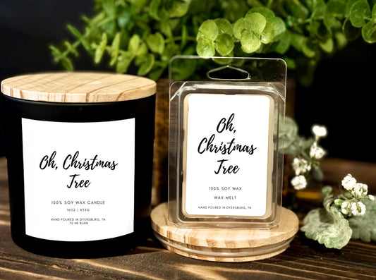 Black candle and wax melt with 'Oh, Christmas Tree' label on a wooden surface with greenery in the background.