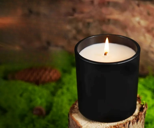 Black candle in a glass holder on a wooden stump with a blurred natural background