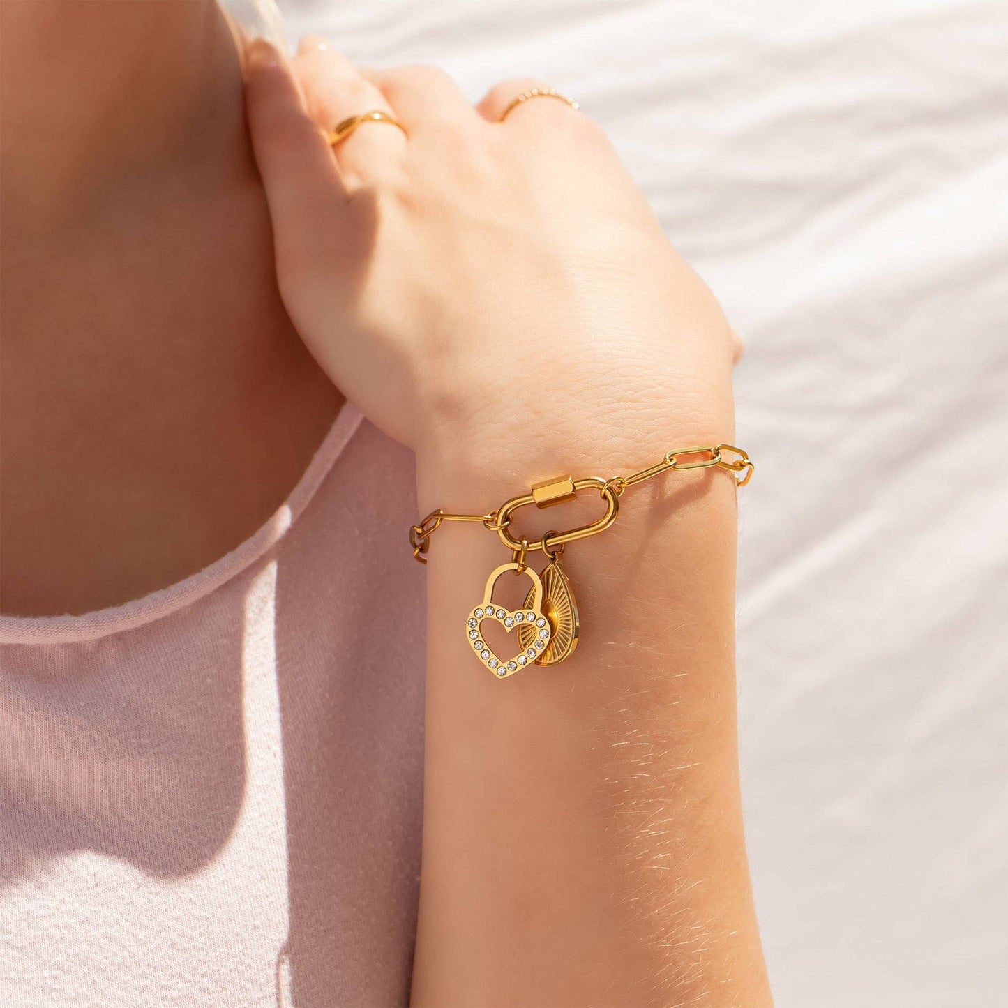 Gold bracelet with heart-shaped charms on a person's wrist against a light background