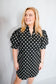 Woman wearing a black polka dot dress against a plain background