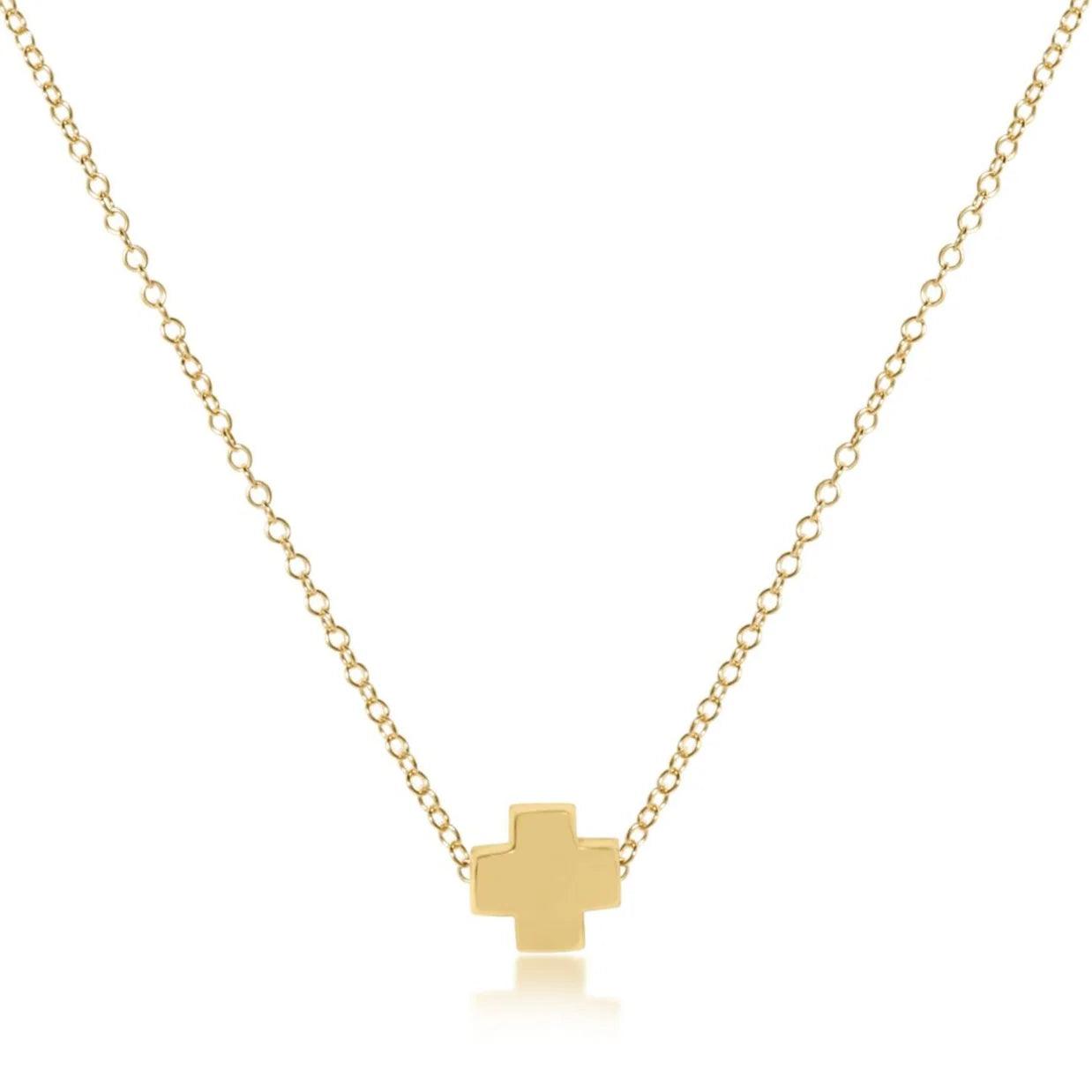 A gold-filled cross necklace on a gold-filled chain, branded by enewton presented against a white background.