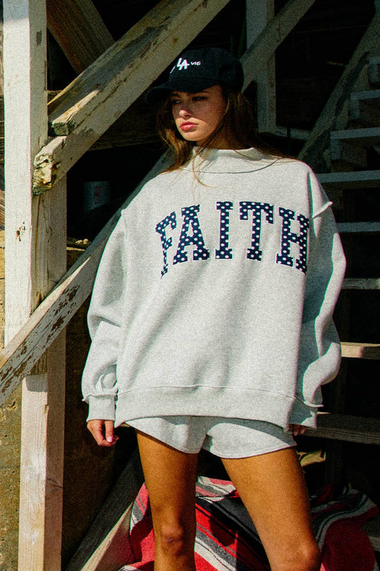 Person wearing a gray sweatshirt with 'FAITH' printed on it, standing in an outdoor setting.