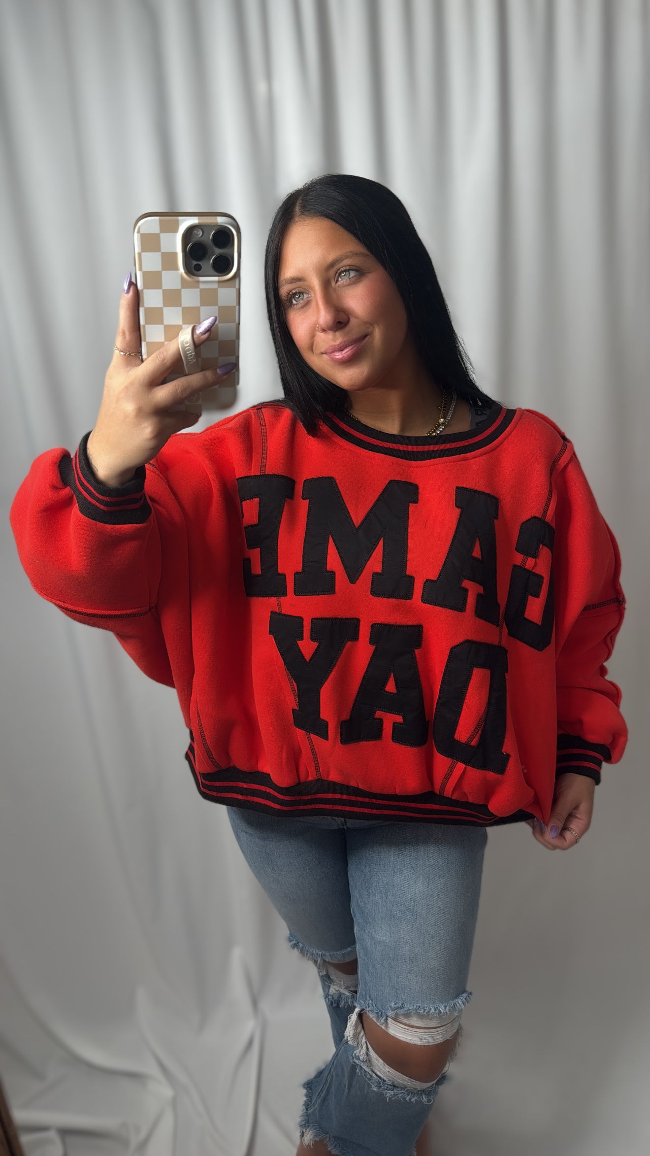 A girl taking a selfie with a red and black game day sweatshirt in a mirror 
