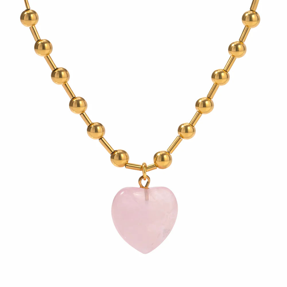 Gold beaded necklace with a pink heart pendant on a white background