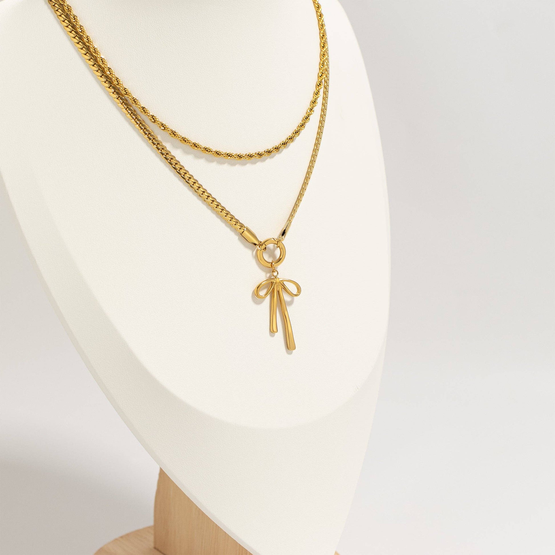Gold necklace with a bow pendant on a white mannequin.