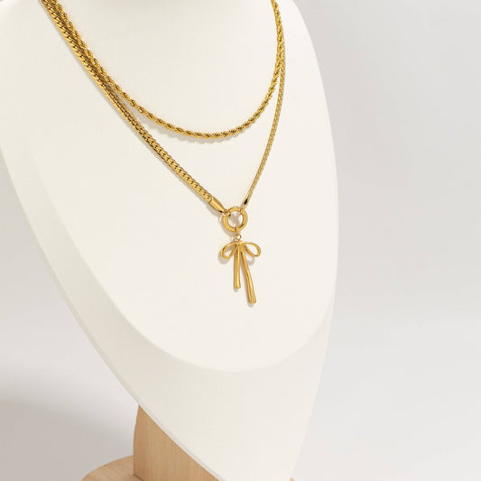 Gold necklace with a bow pendant on a white mannequin.
