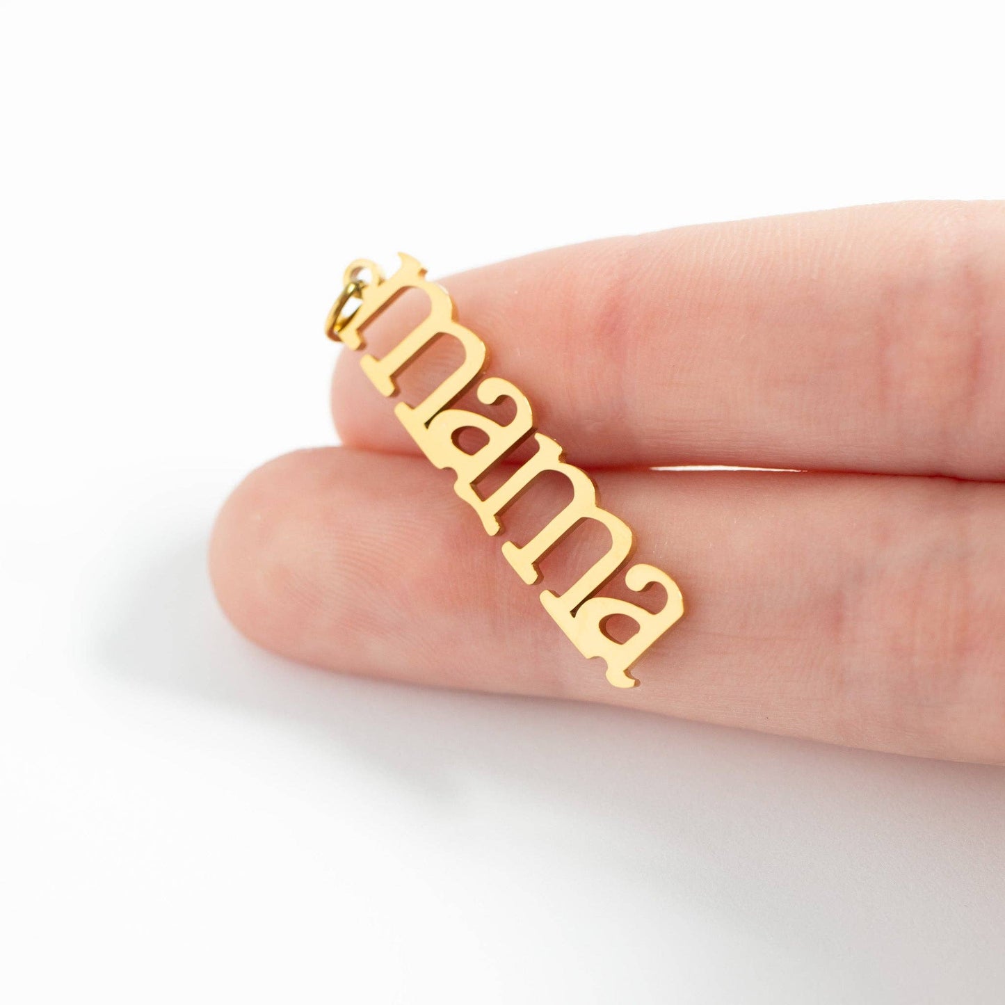Gold 'mama' pendant held between fingers on a white background