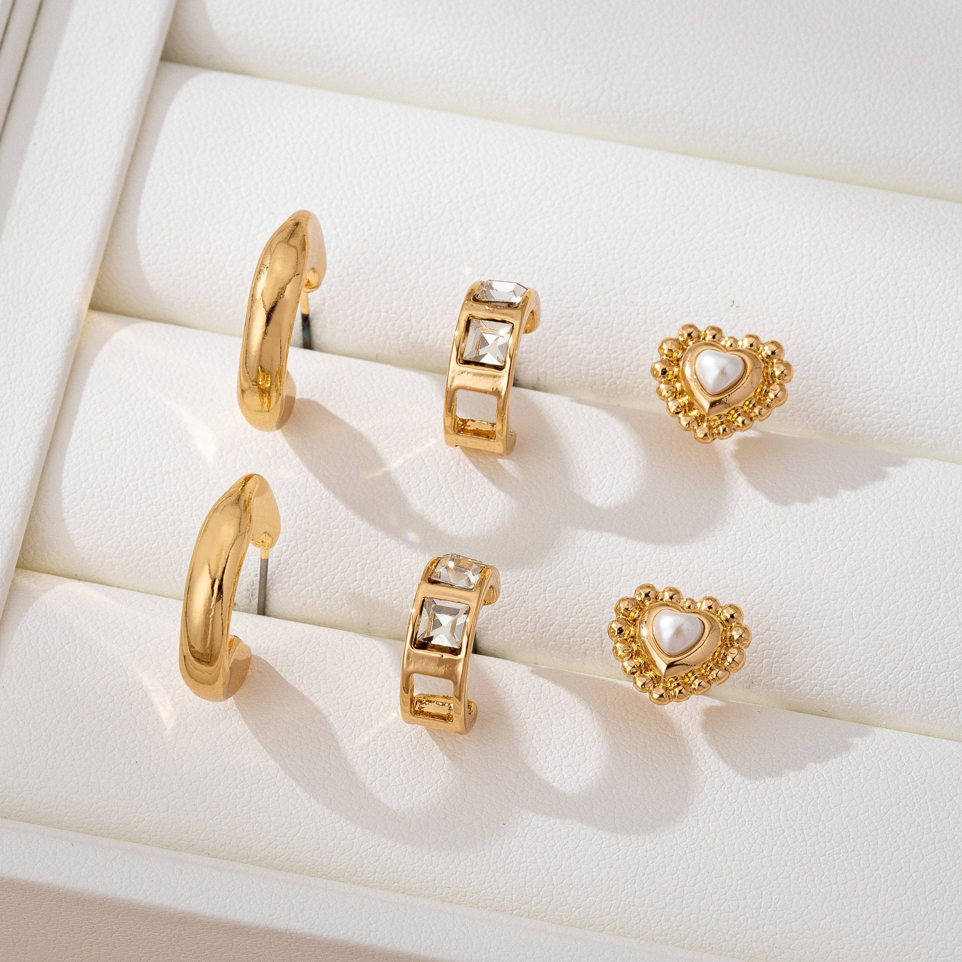 Gold earrings with heart and hoop designs on a white cushioned surface
