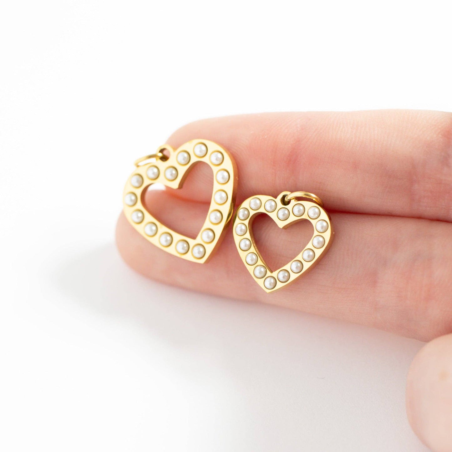 Gold heart-shaped earrings with pearl accents held between fingers on a white background