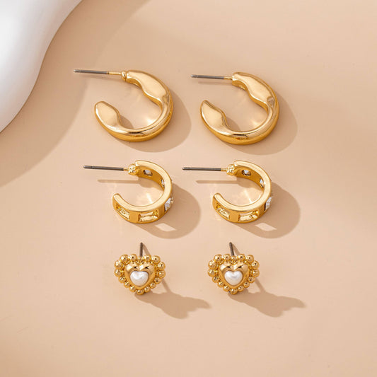 Set of gold hoop earrings and heart-shaped earrings on a beige background