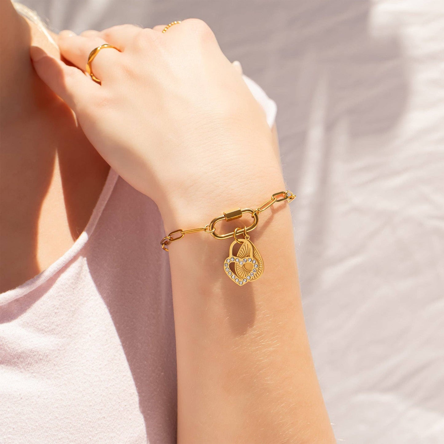 Gold bracelet with a heart-shaped charm on a person's wrist against a neutral background