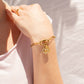 Gold bracelet with a heart-shaped charm on a person's wrist against a neutral background