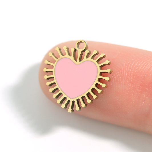 Gold heart-shaped pendant with pink center on a finger