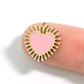 Gold heart-shaped pendant with pink center on a finger