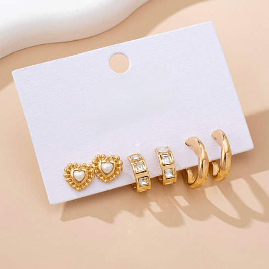 Set of gold earrings on a white card with a beige background