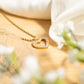 Gold heart-shaped necklace with clear stones on a wooden surface with white flowers.