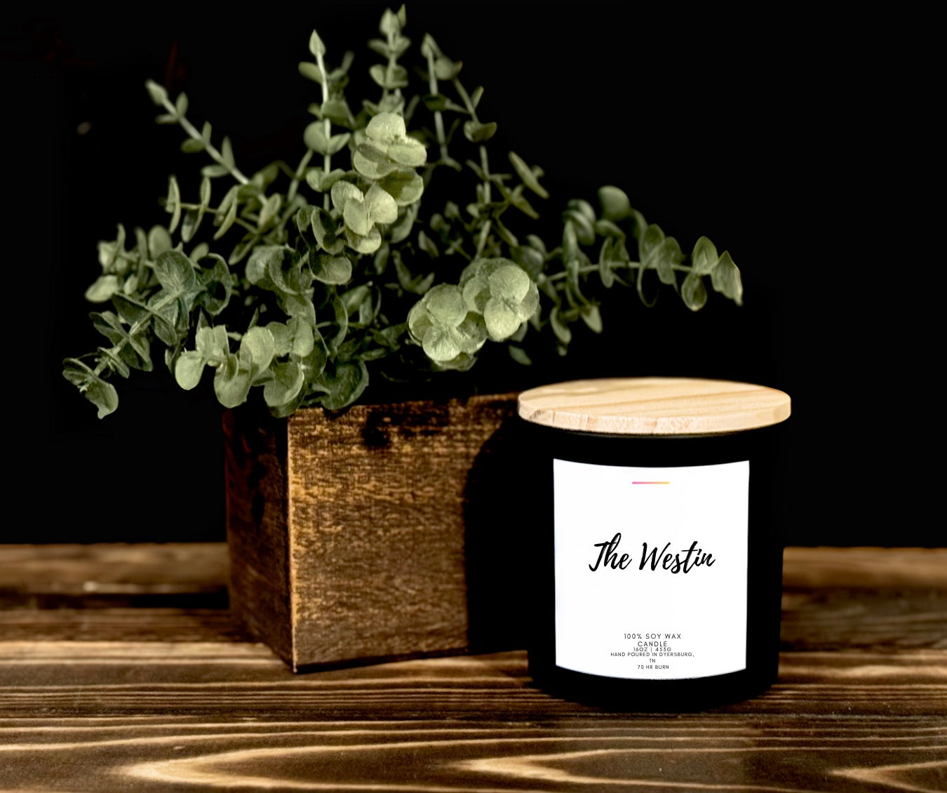 Candle labeled 'The Westin' with a plant on a wooden surface