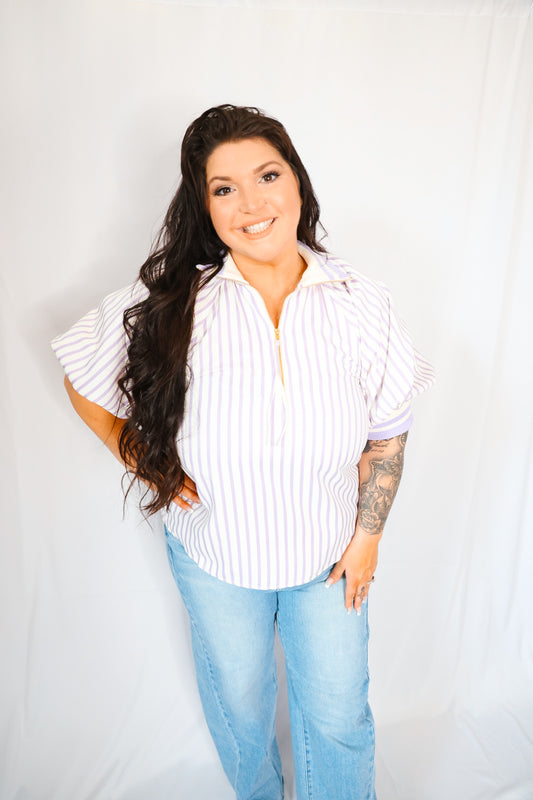 Woman wearing a lavender and white striped shirt and blue jeans against a plain background