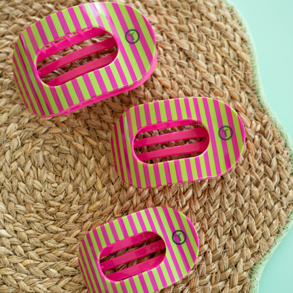 Three pink and green striped hair clips on a woven surface.