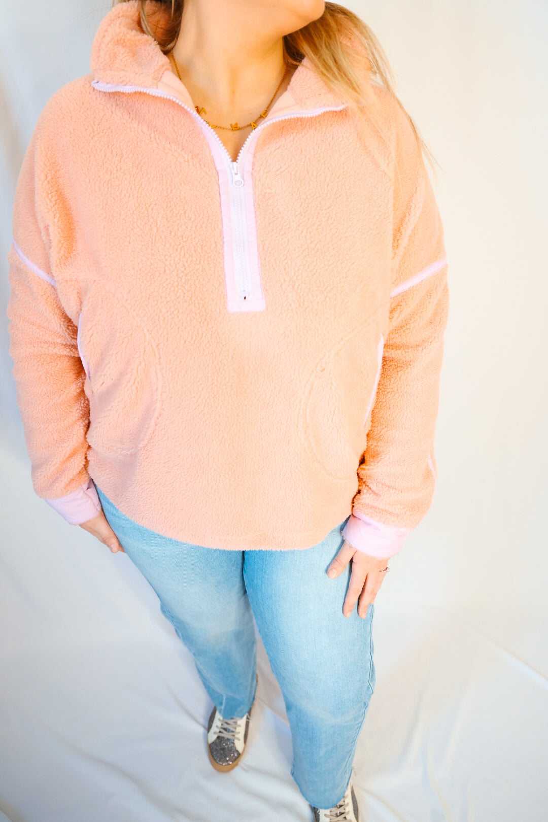 Person wearing a peach fleece pullover with white zipper and light blue jeans on a plain background