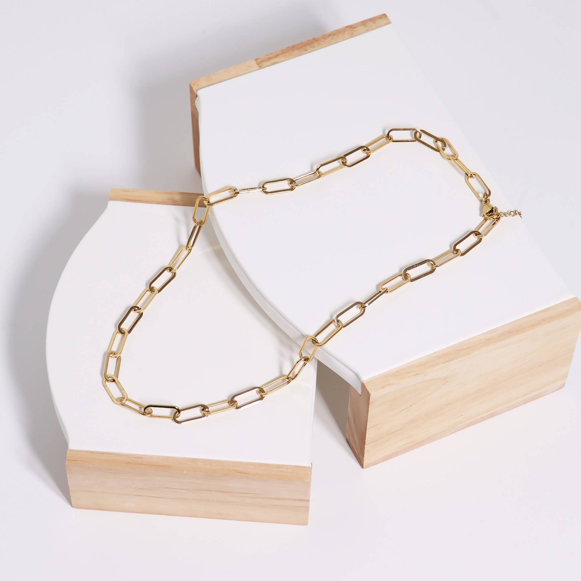 Gold chain necklace on a white and wooden stand against a light gray background