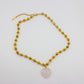 Gold beaded necklace with a heart-shaped pink stone pendant on a light gray background