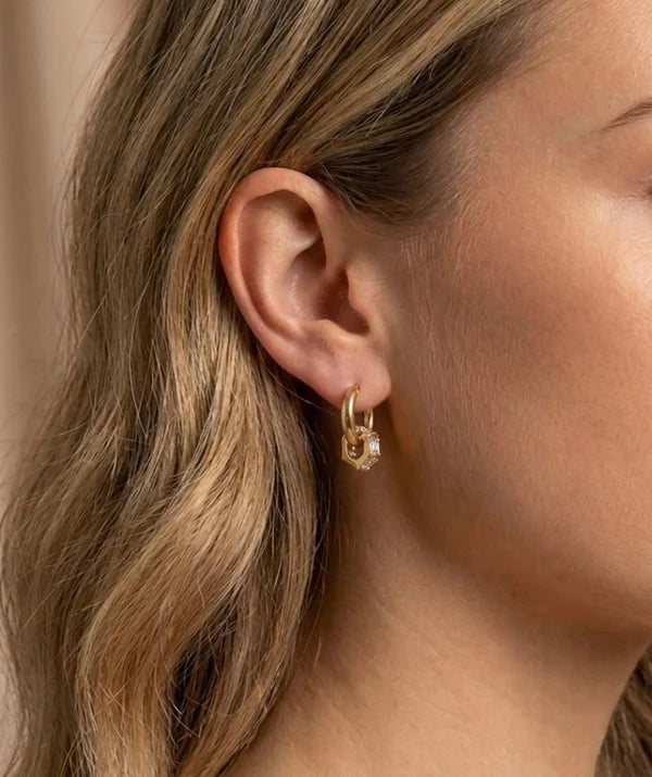 Close-up of a person wearing a gold hoop earring with a small diamond.