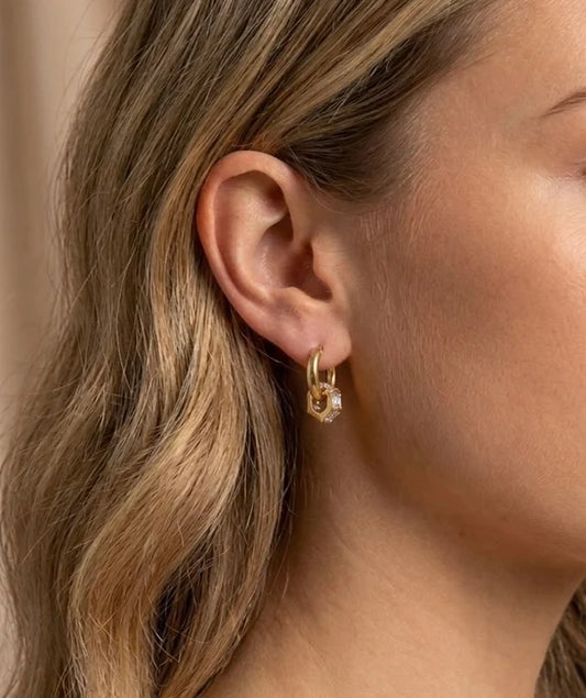 Close-up of a person wearing a gold hoop earring with a small diamond.