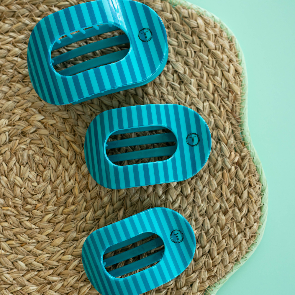 Three blue striped hair clips on a woven mat with a light green background