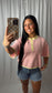 A woman takes a mirror selfie wearing a pink and white striped short-sleeve henley shirt with yellow-green trim, paired with denim shorts, in front of a white curtain backdrop.