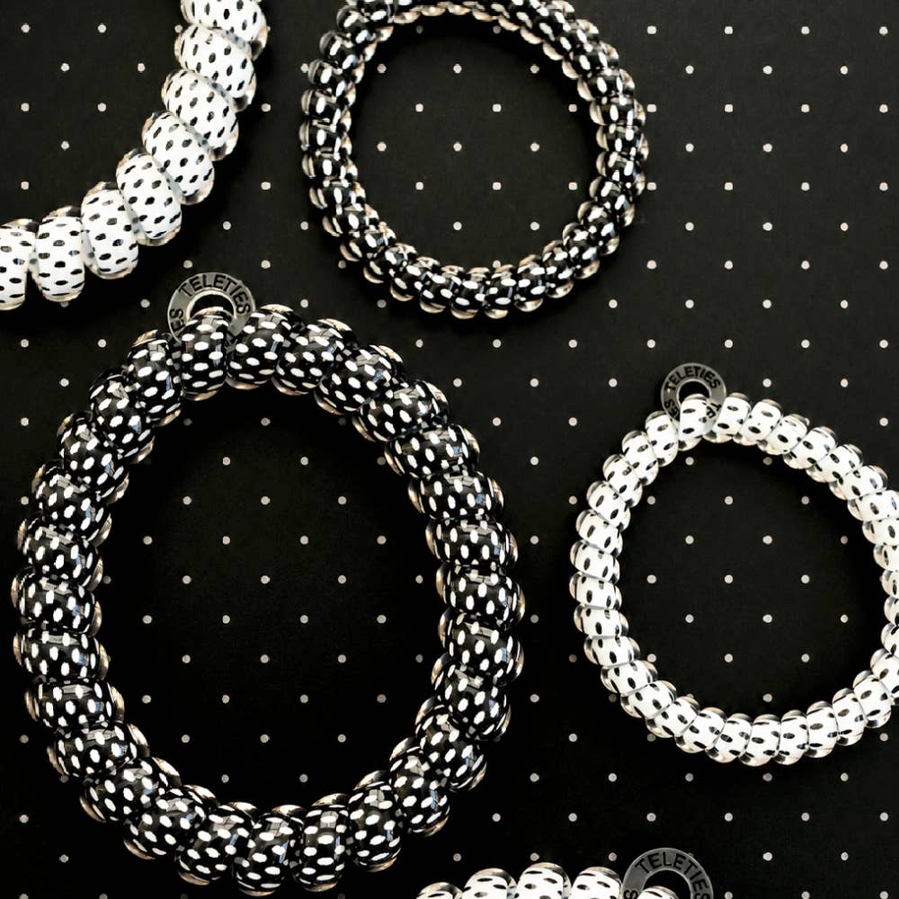 Four plastic elastic bracelets in white and black, arranged on a black background with a white polka-dot pattern. 
