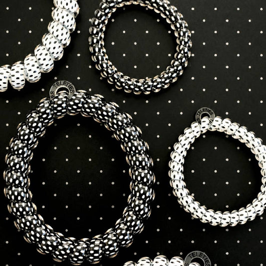 Four plastic elastic bracelets in white and black, arranged on a black background with a white polka-dot pattern. 