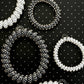 Four plastic elastic bracelets in white and black, arranged on a black background with a white polka-dot pattern. 