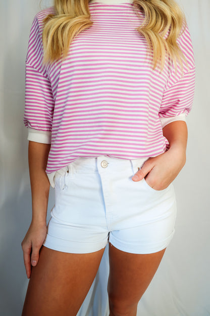 Person wearing a pink and white striped shirt and white shorts against a plain background