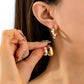 Close-up of a person wearing gold hoop earrings with pearl accents.