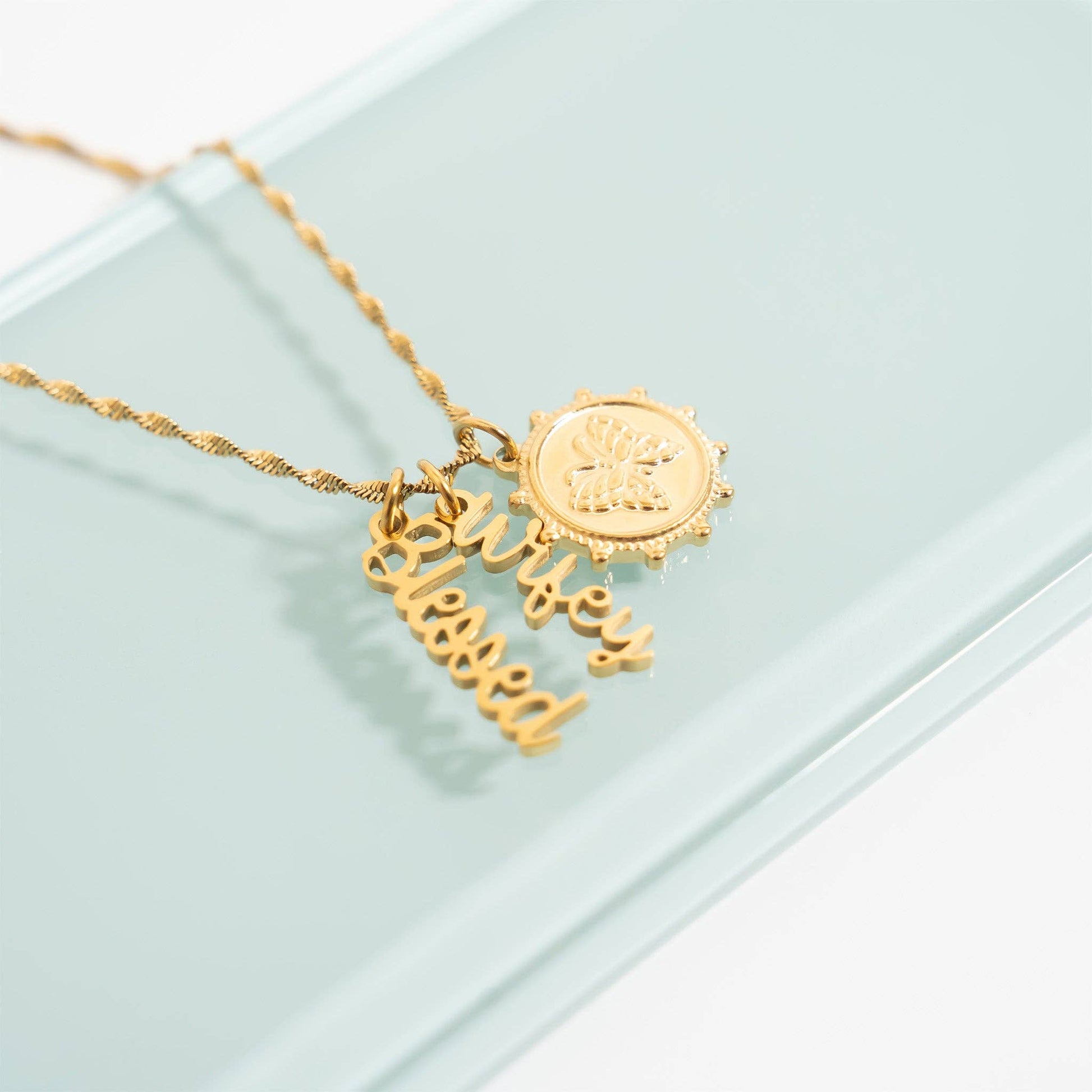 Gold necklace with 'blessed' pendant on a light green background