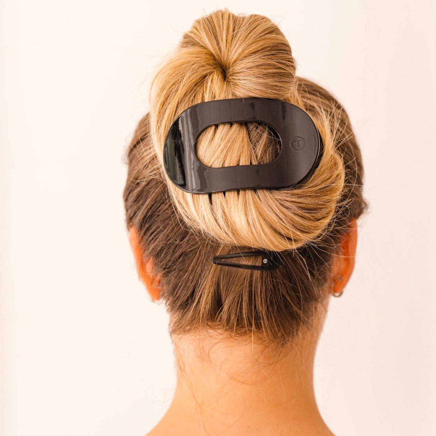 Person with a bun holding a black hair clip against a plain background
