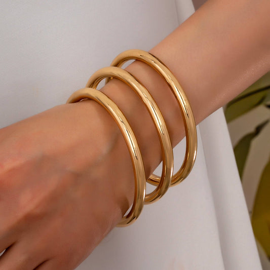 Gold bangles on a wrist against a neutral background