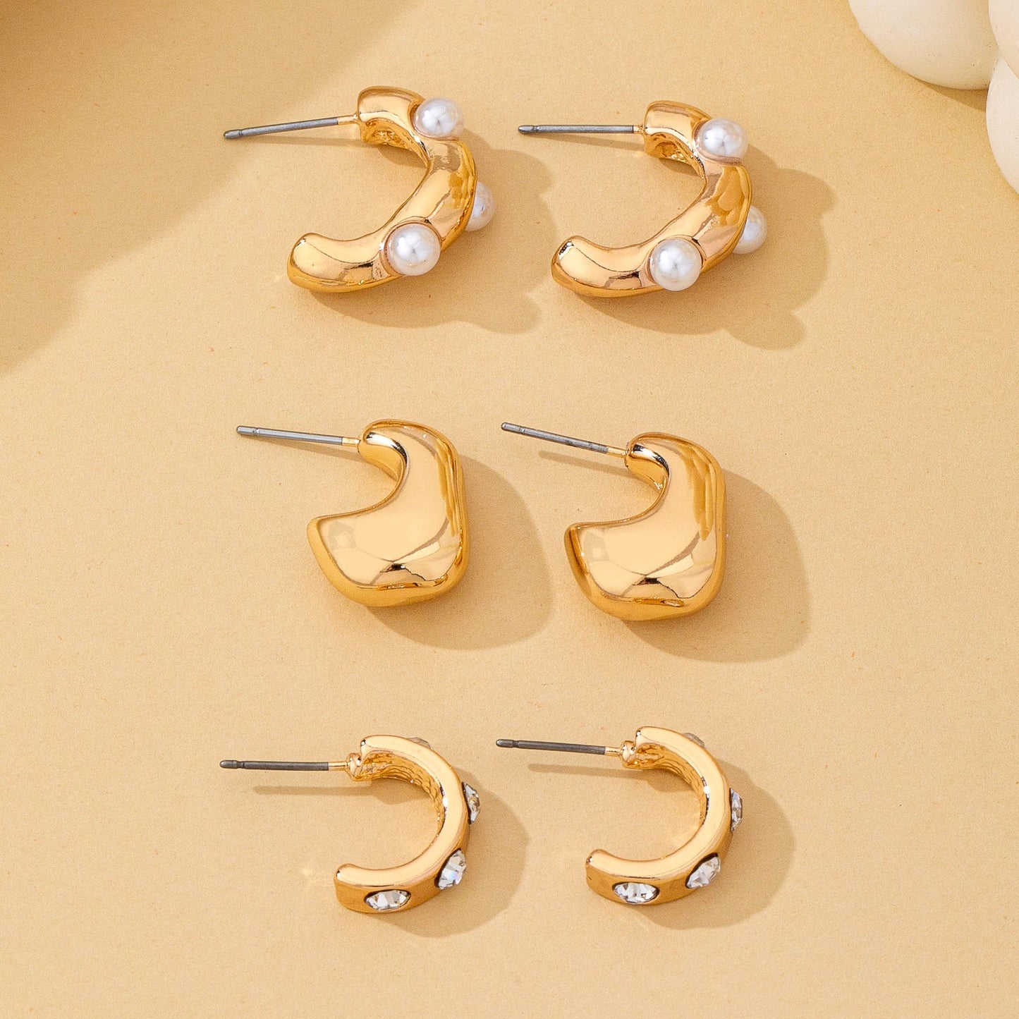 Gold hoop earrings with pearl and gemstone accents on a beige background