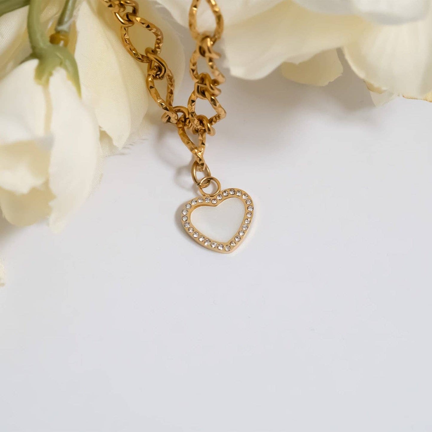 Gold chain bracelet with a heart-shaped charm on a white background with flowers.