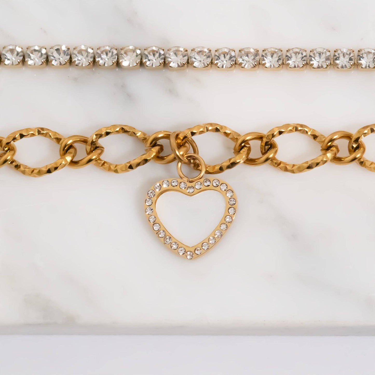 Gold bracelet with heart charm and clear gemstones on a white marble surface